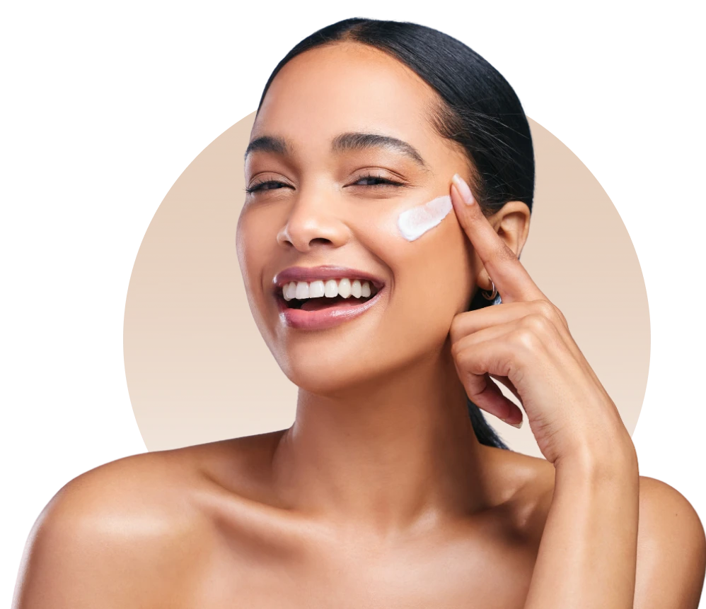 Smiling person applying face cream, dark background.